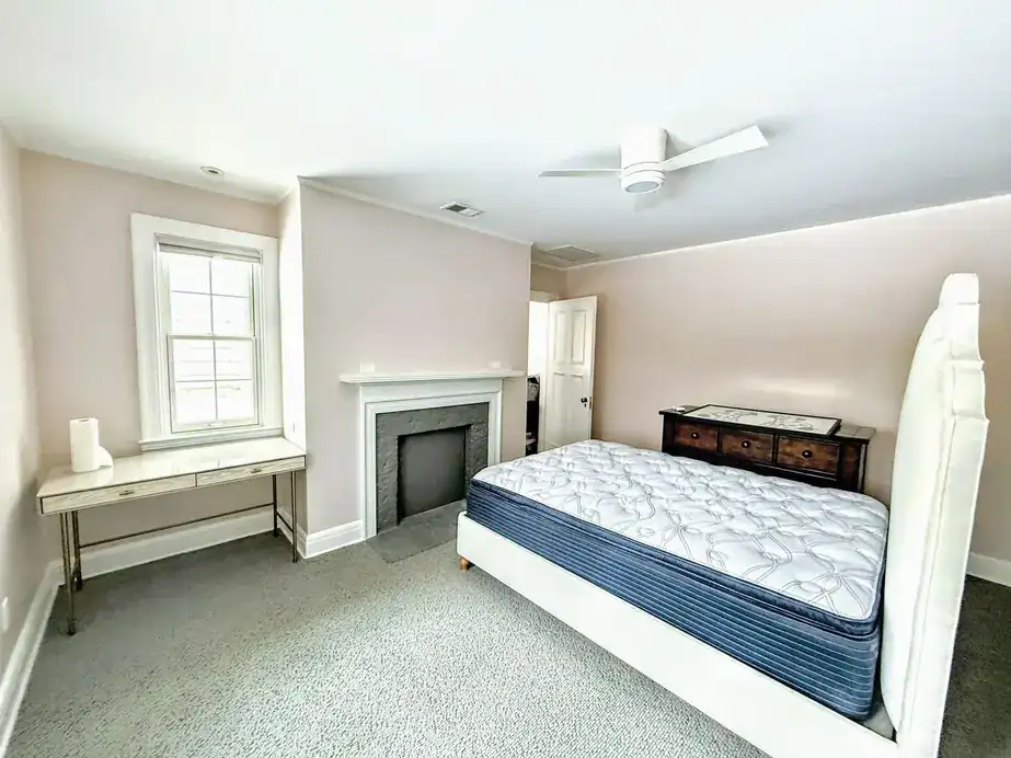 The same bedroom with a white fireplace against blush-grey walls